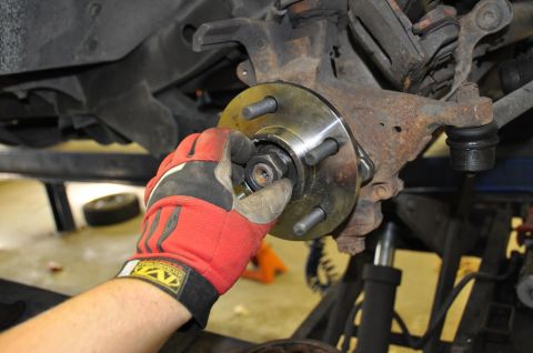1996 Ford Bronco - Mechanic works on a vehicle's wheel hub assembly, tightening a nut with a gloved hand.