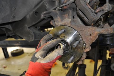 1996 Ford Bronco - Mechanic's hands installing a new wheel hub assembly onto a vehicle's suspension.