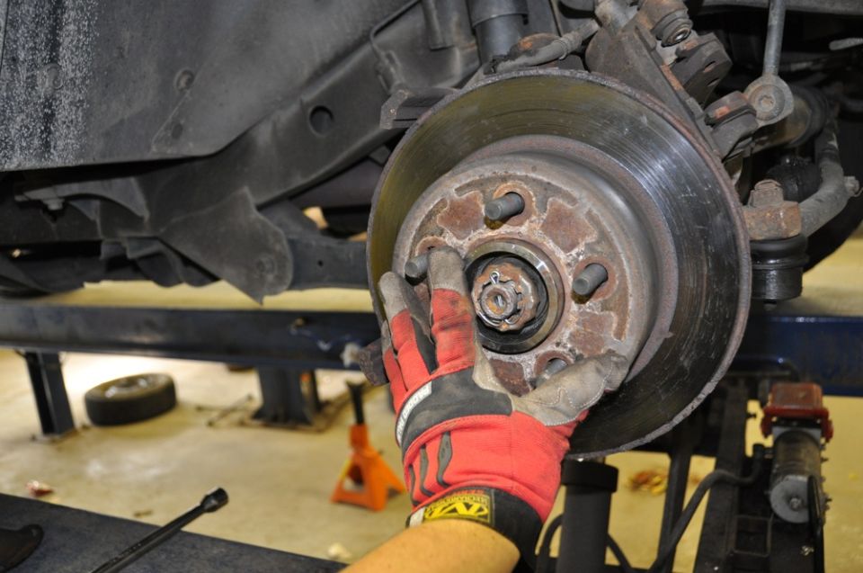 Gloved hand working on a rusty wheel hub assembly