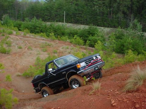1989 Ford Bronco - This black SUV is navigating a challenging off-road terrain on a dirt incline.