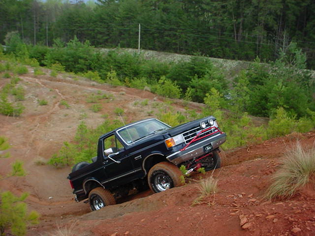 Black SUV climbing a steep dirt hill with trees in the background