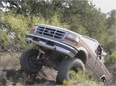 1996 Ford Bronco - A tan Ford Bronco is shown tilted on a dirt incline with its front grille and bumper visible.