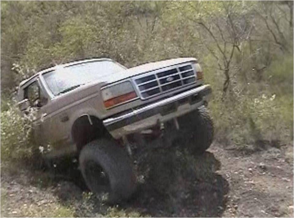 Ford Bronco with large tires driving up a dirt hill, front grille visible