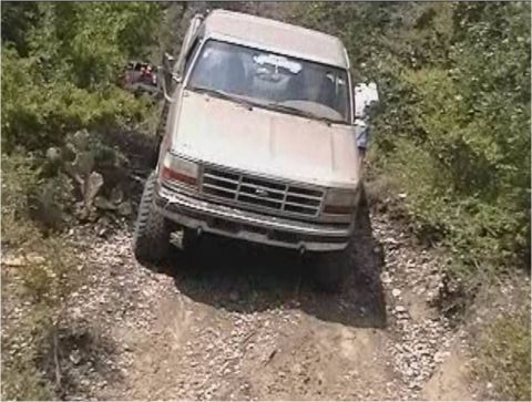 1996 Ford Bronco - This Ford Bronco is navigating a rough, unpaved trail surrounded by dense vegetation.