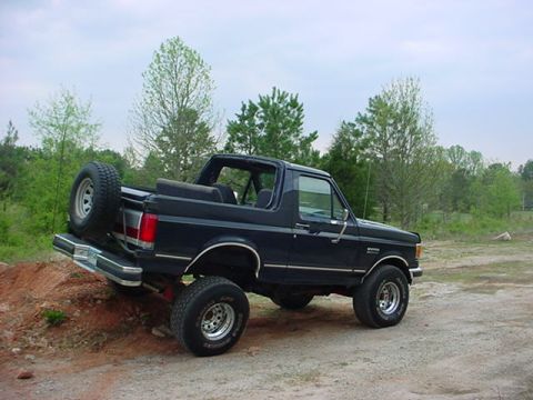 1989 Ford Bronco - A black Ford Bronco is shown from a three-quarter front view, parked on a dirt embankment.