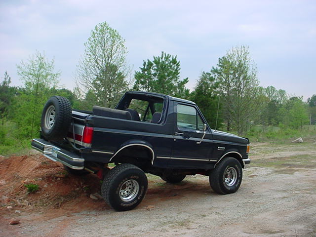 Black Ford Bronco with a spare tire mounted on the rear, angled on a dirt incline