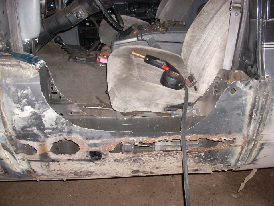Interior and rusted rocker panel of a classic SUV, with a welding torch.