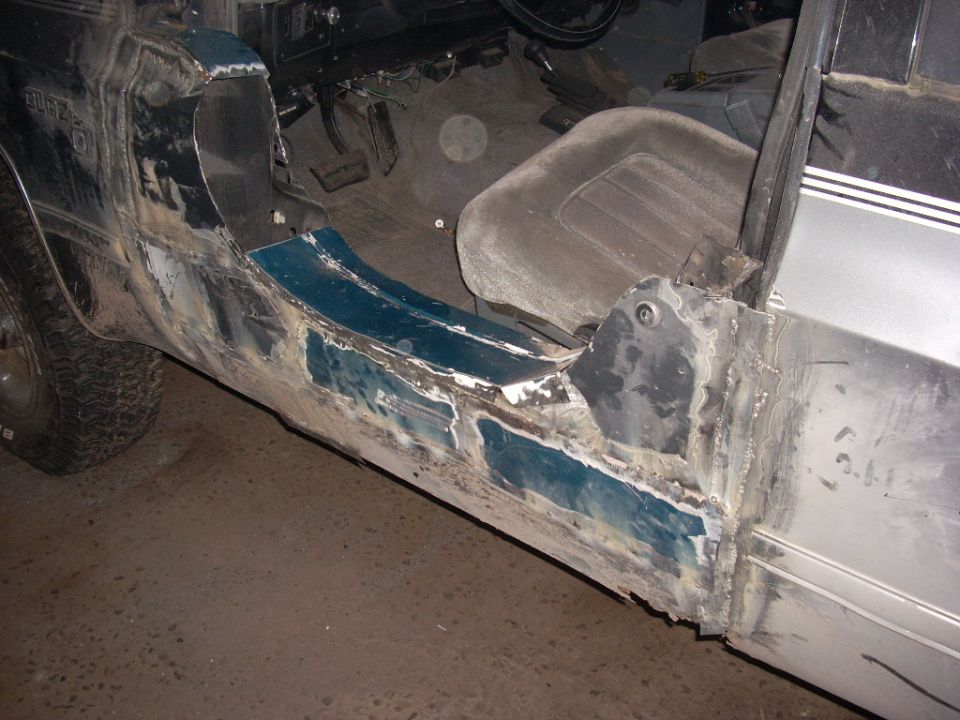 Close-up of a classic SUV's driver side rocker panel with visible welding and repair work.