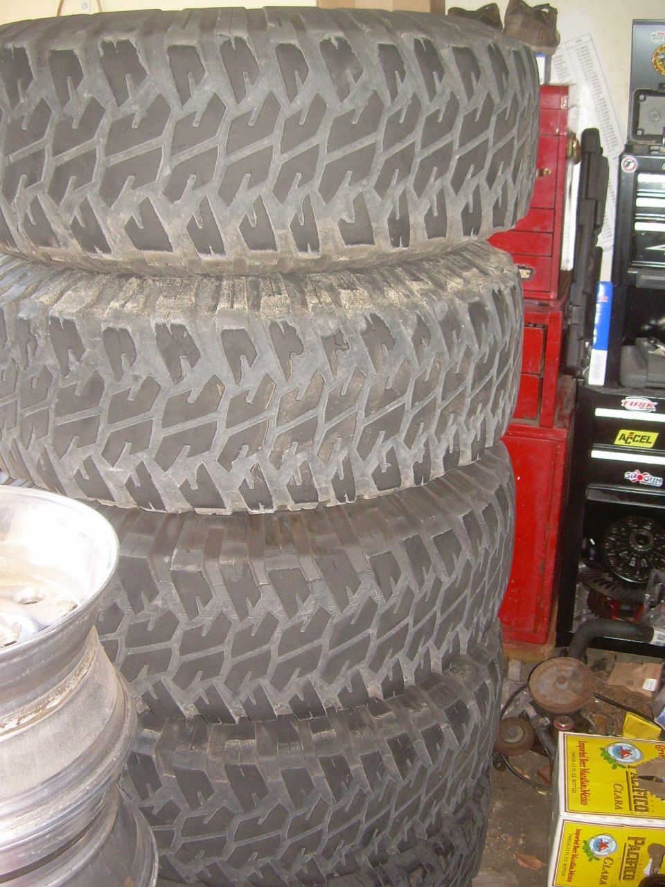 Stack of four off-road tires with aggressive tread, silver wheel rim visible.