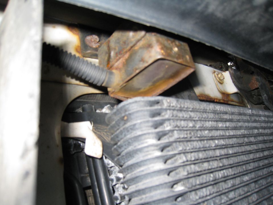 Stacked-plate cooler and rusty bracket ahead of a radiator inside an engine bay