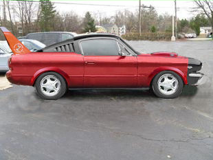 1986 Ford Bronco - A custom red coupe with a black roof and a prominent orange fin on the rear quarter panel is parked on an asphalt lot.