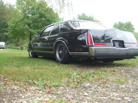 1996 Ford Bronco - The rear driver's side quarter view of a black Lincoln Mark VII is shown parked on a grassy area with a gravel path in the foreground. The…