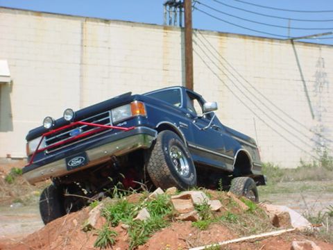 1989 Ford Bronco - This blue Ford truck is navigating a rocky incline, its off-road capabilities.