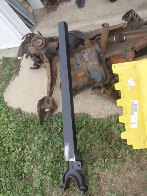 1996 Ford Bronco - A black painted metal part, likely a suspension component, is laid out on the ground next to rusty vehicle parts and a yellow plastic bin.…