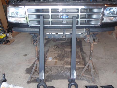 1996 Ford Bronco - The front of a 1996 Ford Bronco is shown on jack stands with the grille and headlights visible. Two black metal support beams are positione…