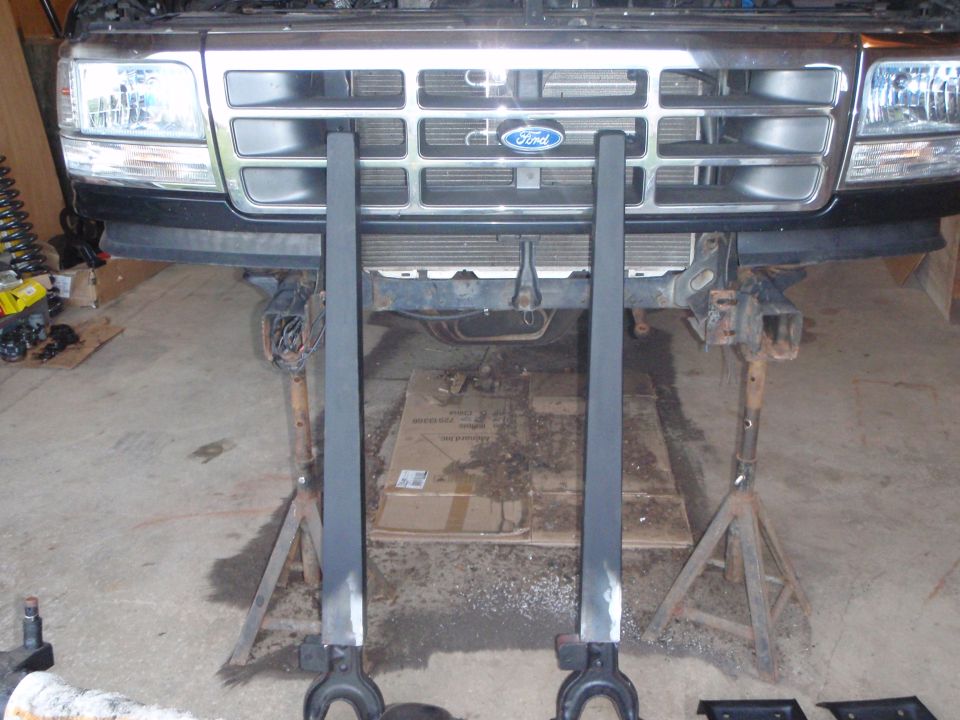 1996 Ford Bronco front end on jack stands with two black support beams in front.