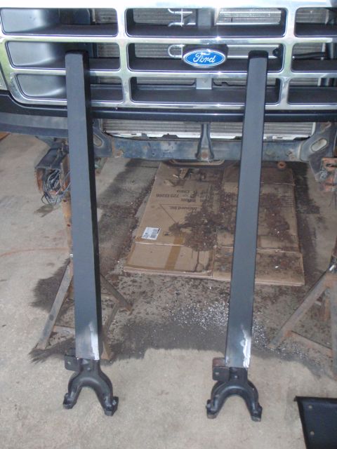 1996 Ford Bronco - Two black metal brackets are positioned in front of a Ford Bronco grille. The brackets are standing upright on the concrete floor, supporte…
