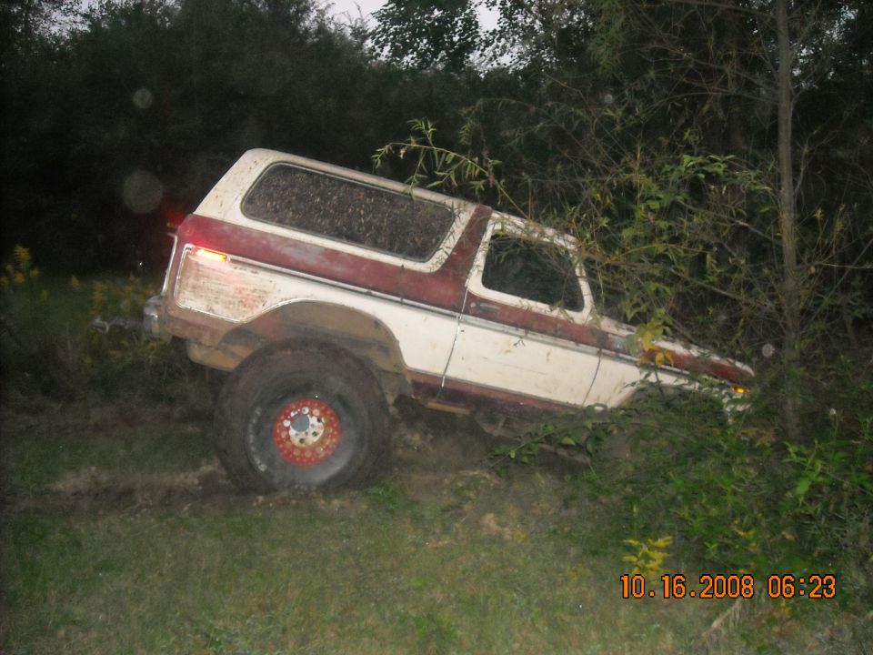1979 Ford Bronco, white and red, parked off-road in trees.