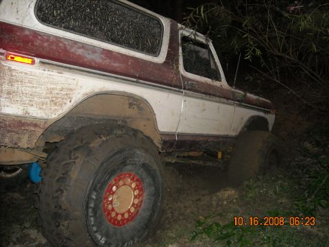1979 Ford Bronco - A mud-covered 1979 Ford Bronco is stuck in thick mud off-road at night. The vehicle's large tires and red-accented rims are visible.