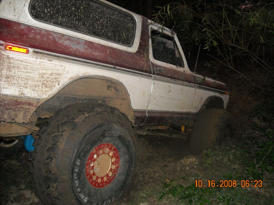 Mud-covered 1979 Ford Bronco stuck in mud off-road at night.