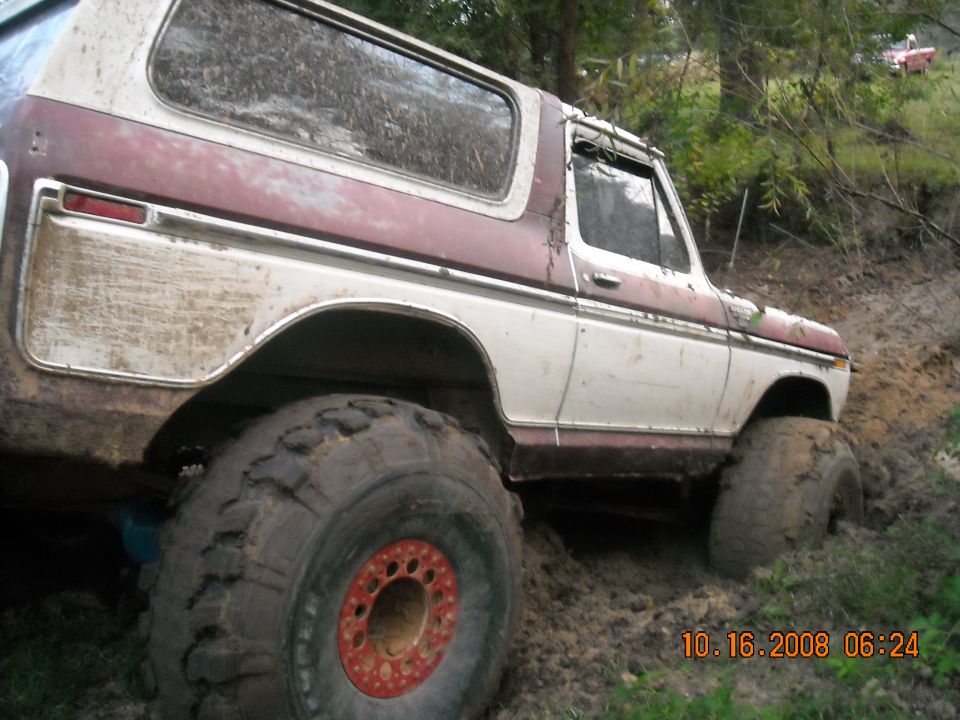 Mud-covered 1979 Ford Bronco stuck in mud, showing large tires and maroon/white paint.