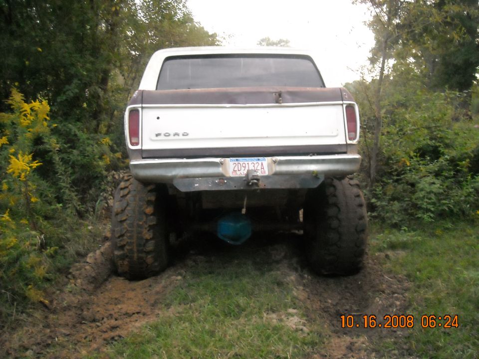 Rear view of a lifted Ford pickup truck with large tires stuck in mud