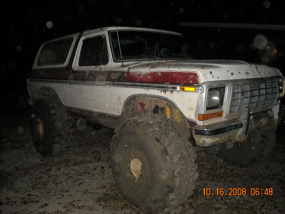 Muddy white and maroon Ford Bronco with large tires, front quarter view