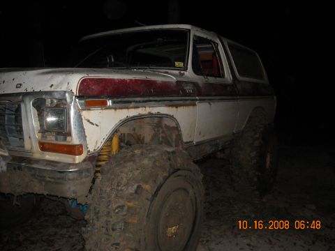 1979 Ford Bronco - Mud-covered Ford Bronco with a red stripe, photographed in low light conditions.