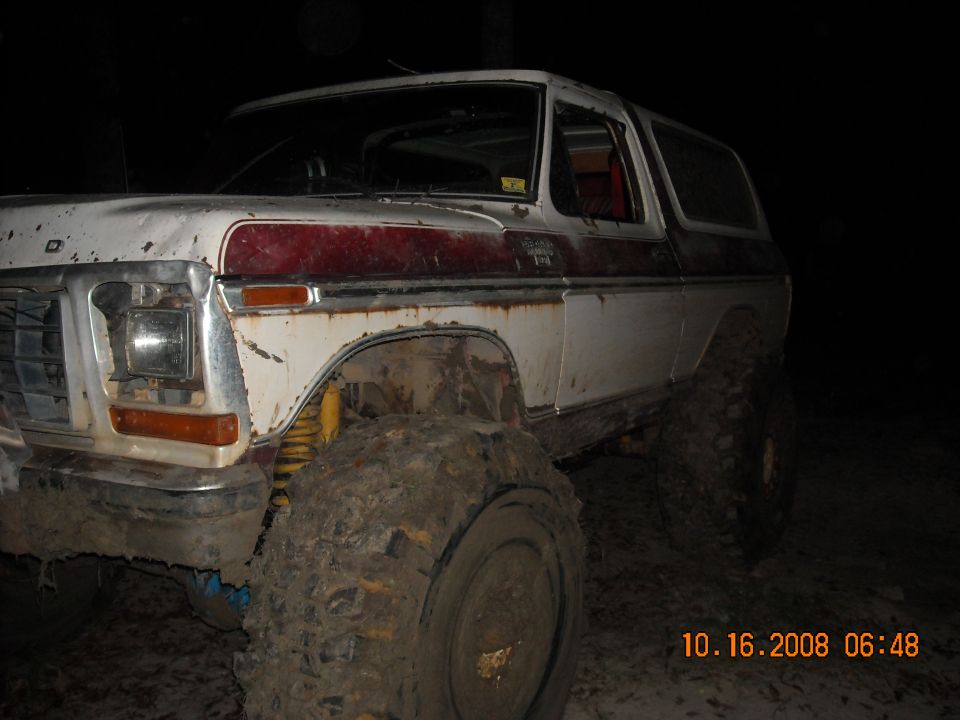 White and red Ford Bronco with mud-caked tires, seen from the front-left