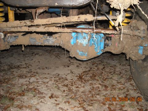 1979 Ford Bronco - Undercarriage of a vehicle heavily coated in mud, showing the front axle and suspension.