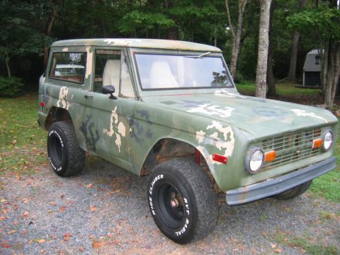 1992 Ford Mustang - An early Ford Bronco (first-generation) two-door SUV shown in a 3/4 front view, wearing a faded green camouflage paint scheme with rust and…