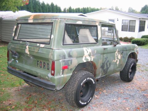 1992 Ford Mustang - Rear three-quarter view of an early Ford Bronco (first-generation) two-door SUV painted in a green, tan and brown camouflage scheme, with '…