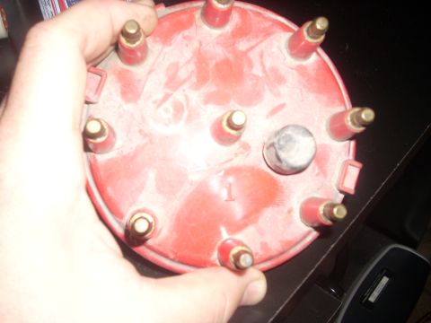 1992 Ford Bronco - A red distributor cap with multiple brass terminals is held by a hand. A number '1' is visible on the cap's surface.
