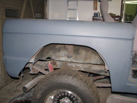 1976 Ford Bronco - The rear fender and wheel well of a vehicle, prepped for paint, reveal suspension details and a tire with a custom rim.