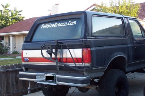 1990 Ford Bronco - The rear of a black 1990 Ford Bronco is shown, a spare tire carrier and a website sticker on the rear window.