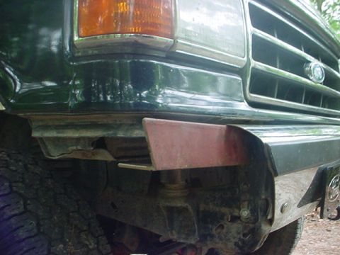 1989 Ford Bronco - Close-up of the front bumper corner on a dark green 1989 Ford Bronco, showing a red tow hook attachment and part of the grille.