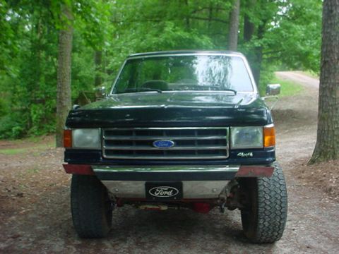1989 Ford Bronco - This Ford truck is parked on a dirt road surrounded by trees.