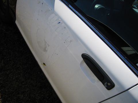 1991 Ford LTD Crown Victoria - The side of a white vehicle displays significant damage and peeling paint around the door handle area.