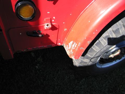 1991 Ford LTD Crown Victoria - Close-up view of the side of a red vehicle, showing wear and tear on the fender and door.