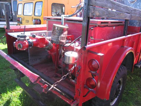 1991 Ford LTD Crown Victoria - Rear view of a red fire truck bed, showing the pump, hoses, and a distinctive can. Other vehicles are visible in the background.