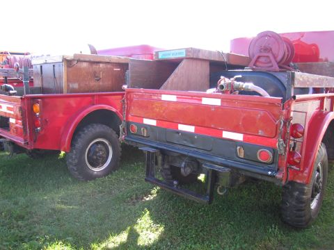 1991 Ford LTD Crown Victoria - Two red military-style trucks are parked side-by-side on a grassy field, both equipped with cargo boxes and hoses.