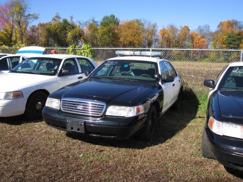 1991 Ford LTD Crown Victoria - A black and white police car is parked in a lot with other vehicles. The number 230 is visible on the windshield.