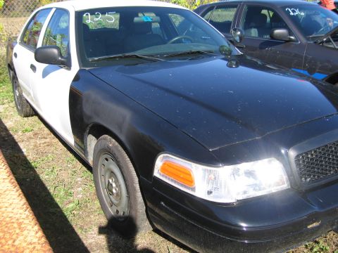 1991 Ford LTD Crown Victoria - A two-tone police car with the number 225 visible on the windshield is parked next to another vehicle.