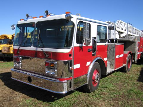 1991 Ford LTD Crown Victoria - A red and white fire truck is parked on a grassy field under a clear blue sky.