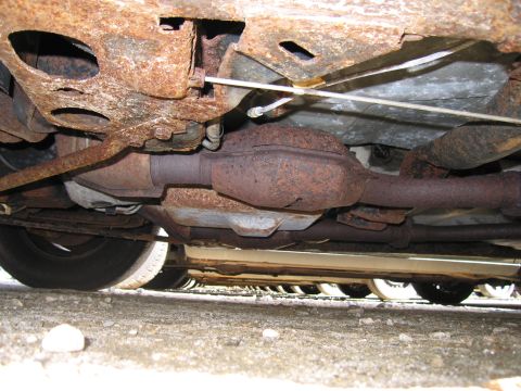 1991 Ford LTD Crown Victoria - The undercarriage of a vehicle displays significant rust and corrosion, with other vehicles visible in the distance.