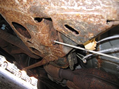 1991 Ford LTD Crown Victoria - The heavily rusted undercarriage of a vehicle is shown, with other vehicles in the background.