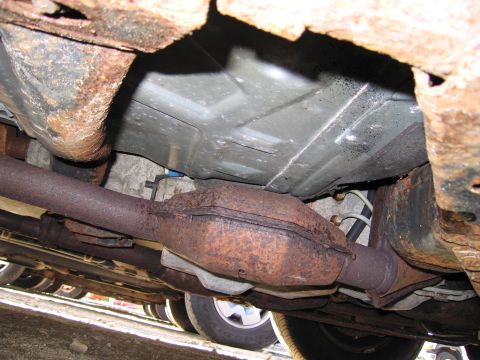 1991 Ford LTD Crown Victoria - Underside view of a vehicle's rusted exhaust system, including the catalytic converter and frame components.