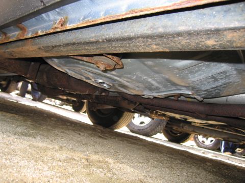 1991 Ford LTD Crown Victoria - The underside of a car reveals significant rust on its frame and exhaust components, with other vehicles parked nearby.