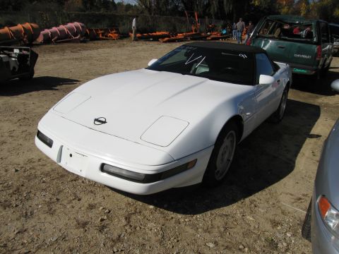 1991 Ford LTD Crown Victoria - A white convertible sports car is parked outdoors with other vehicles and equipment in the background.