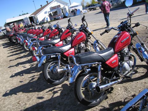 1991 Ford LTD Crown Victoria - Several red Suzuki motorcycles are lined up in a row on a sunny day.